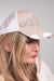 A close up side view of our model, Stephanie, wearing a beige and white trucker style baseball cap with a distressed bill and a large rhinestone and pearl embellished design on the front.