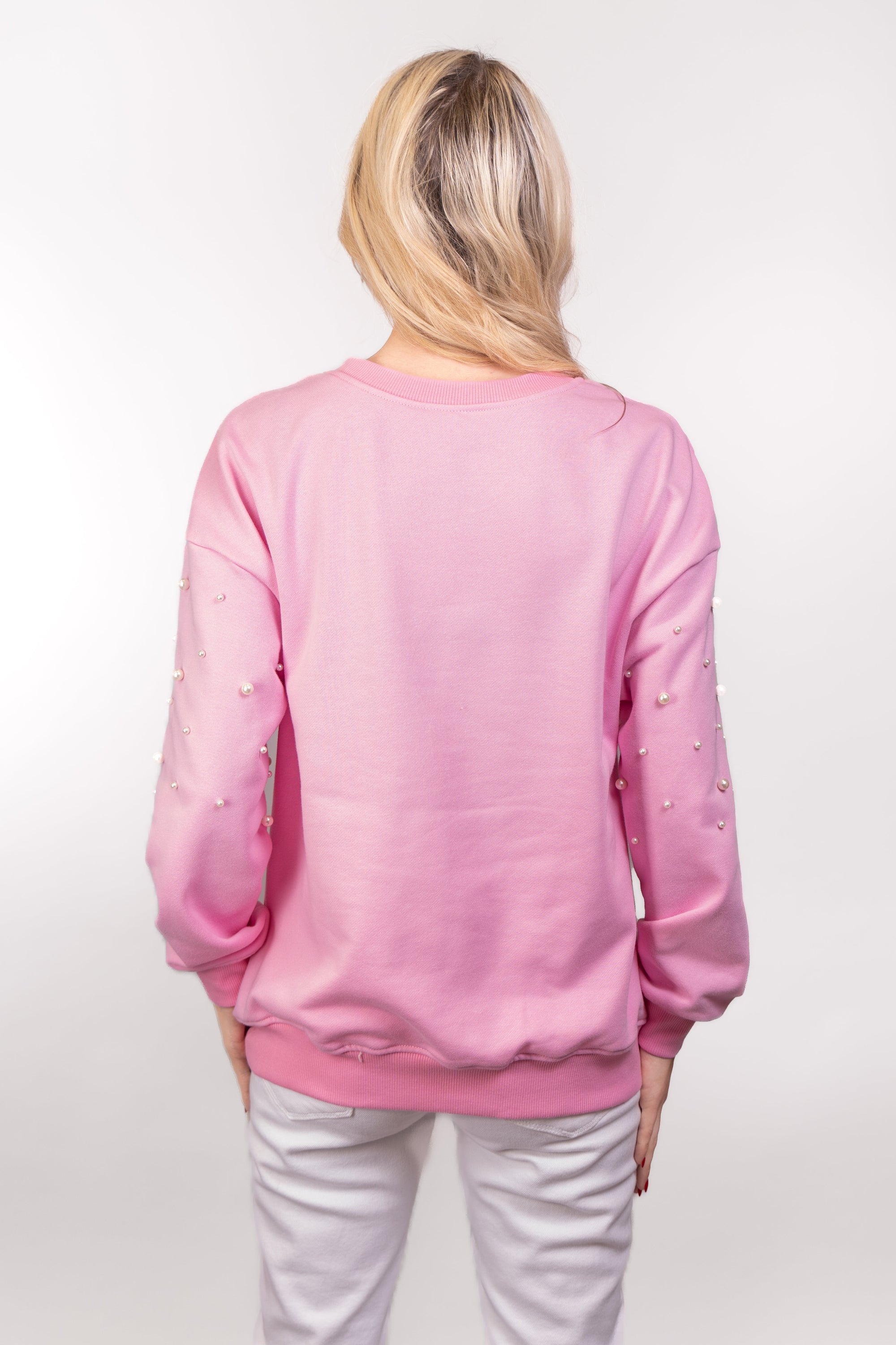 A close-up, back view of our model, Lexi, wearing a baby pink sweatshirt, tastefully embellished with white pearls on the front and sleeves. The back doesn't have any pearls.