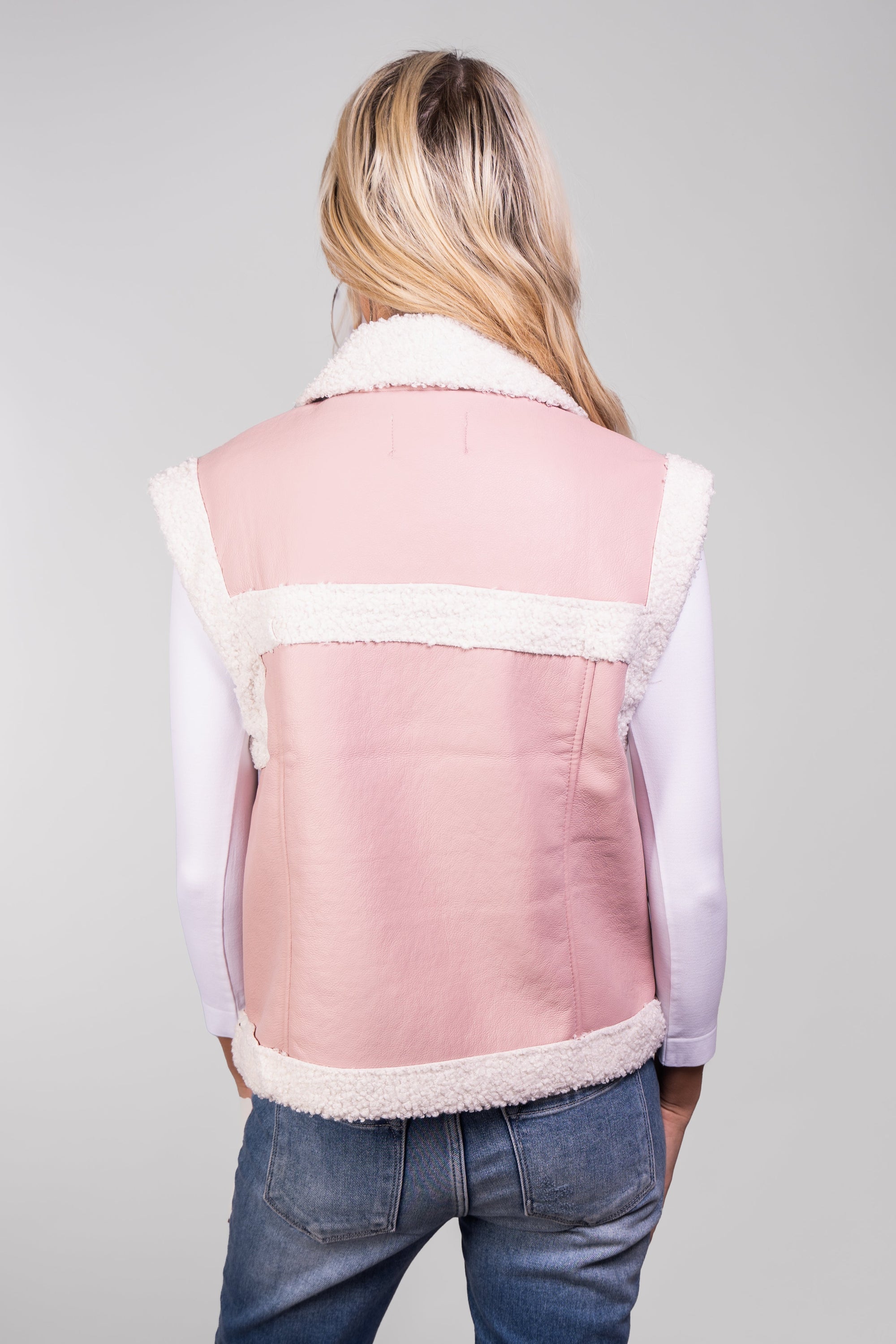 A close-up, back view of our model, Lexi, wearing a light pink faux-leather vest with white sherpa trim.