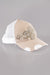 A side view of a beige and white trucker style baseball cap with distressed bill and a bold embellishment of rhinestones and pearls on the front.