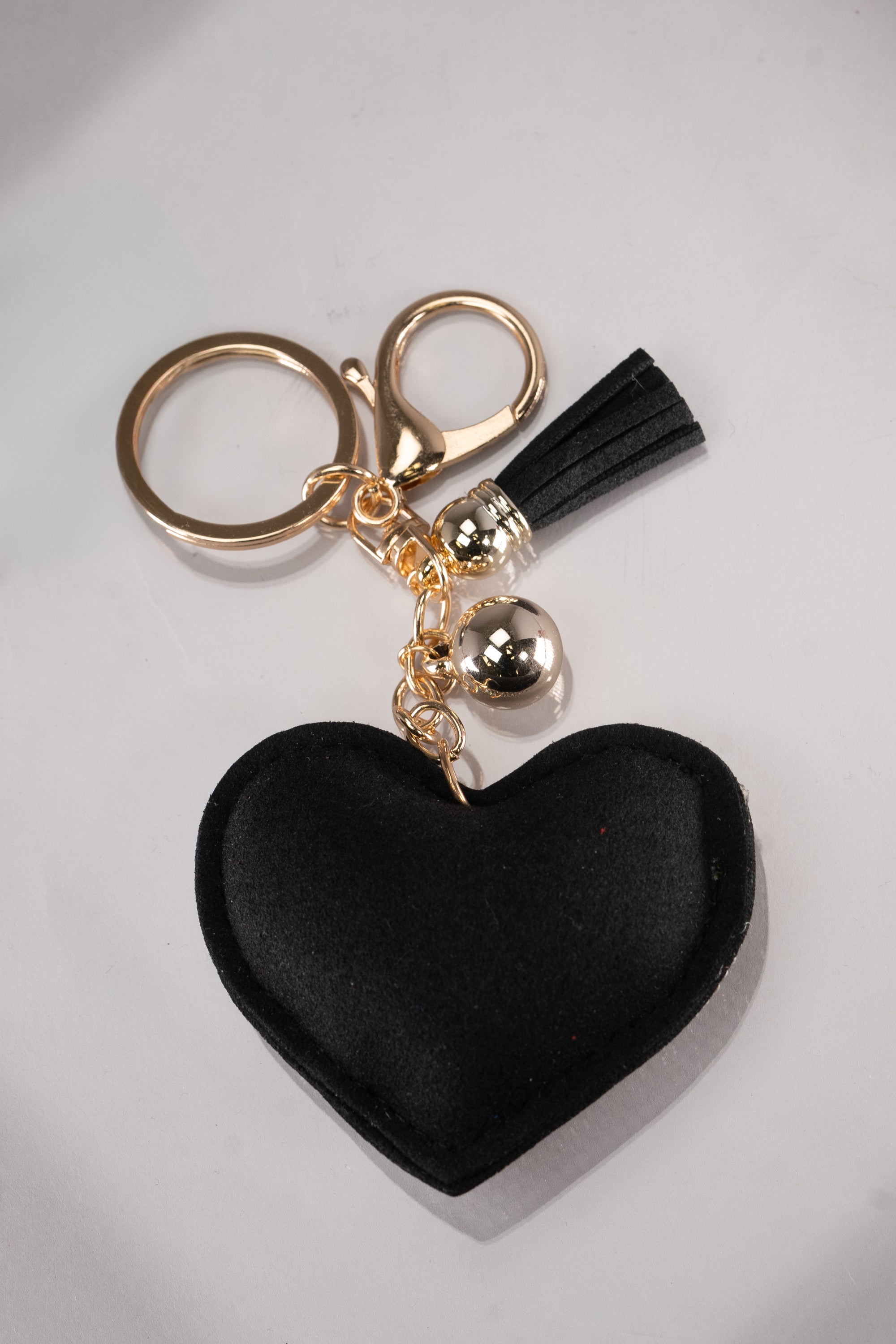 A front view of a black puffy heart keychain with silver rhinestone embellishment and a cute face design on the front, made up of black rhinestone eyelashes and red rhinestone lips in the shape of a heart. This keychain also has gold hardware.