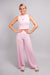 A full body, side view of our model, Lexi, wearing the crinkled sleeveless cropped top and wide leg pants set in light pink. This set is paired with a pink and white ombre rhinestone heart necklace, silver rhinestone earrings, and ivory slide sandals with pearl and rhinestone embellishments.