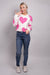 A full body, front-facing view of our model, Lexi wearing a white crew neck sweater with large pink hearts all over. Paired with blue jeans, pink and white ombre earrings, and white rhinestone sneakers for a casual look.