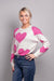 A close-up, front-facing view of our model, Lexi, wearing a white crew neck sweater covered in large pink hearts all over. Paired with blue jeans,  and pink and white ombre rhinestone heart earrings for a casual look.