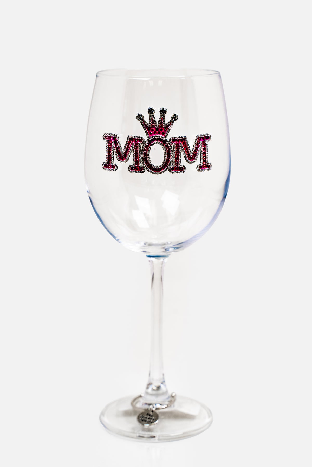 A wine glass with pink and silver rhinestone embellishment on the front, the design says &#39;MOM&#39; in bold serif font and has a crown above the &#39;O&#39;. This glass also has a charm on the stem, resting on the base, which is silver and says &#39;The Queen&#39;s Jewels&#39;.