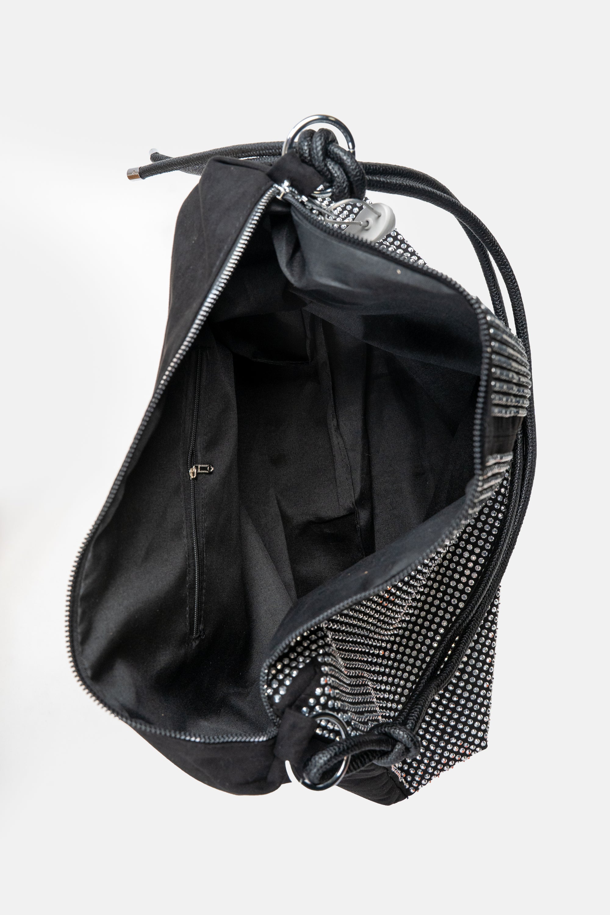 An above view of a large black handbag with silver rhinestone embellishment on the front and a black leather cord strap. This bag also features silver hardware and a long silver zipper on top. This view is showing the spacious interior, black lining, and inner back zipper pocket.