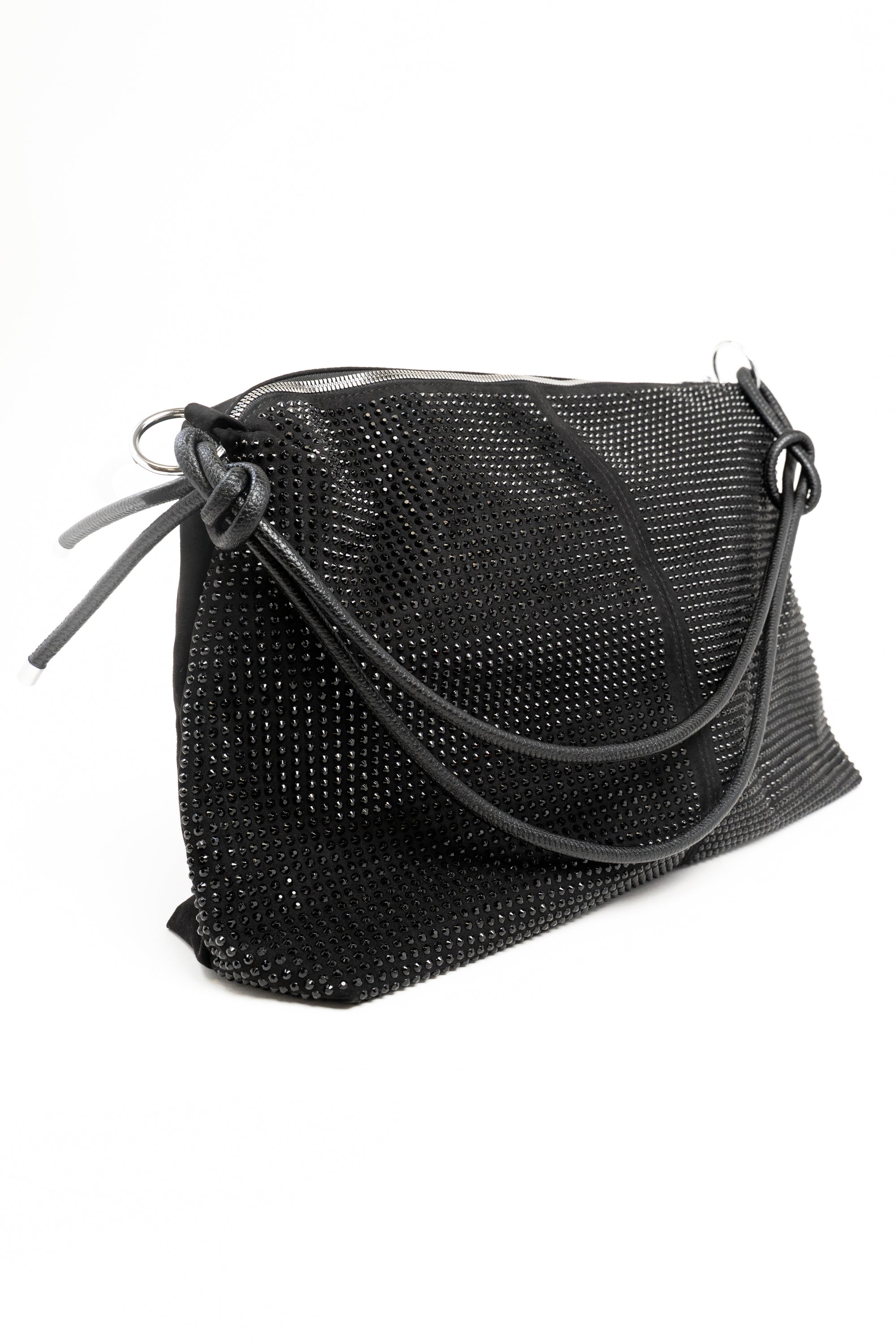 A 3/4 view of a large black rhinestone embellished handbag with a leather cord strap. This bag also features silver hardware and a long silver zipper on top. This view has the strap resting on the front of the bag.