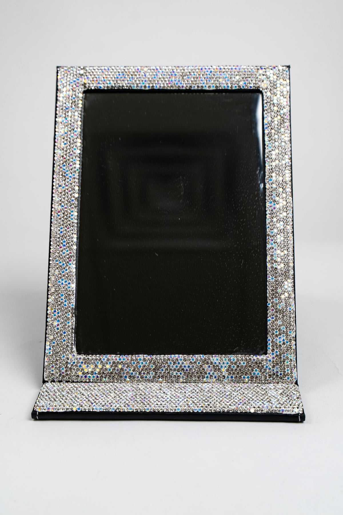 A front view of a large fold-up mirror, in black, with silver and AB rhinestone embellished trim around the mirror