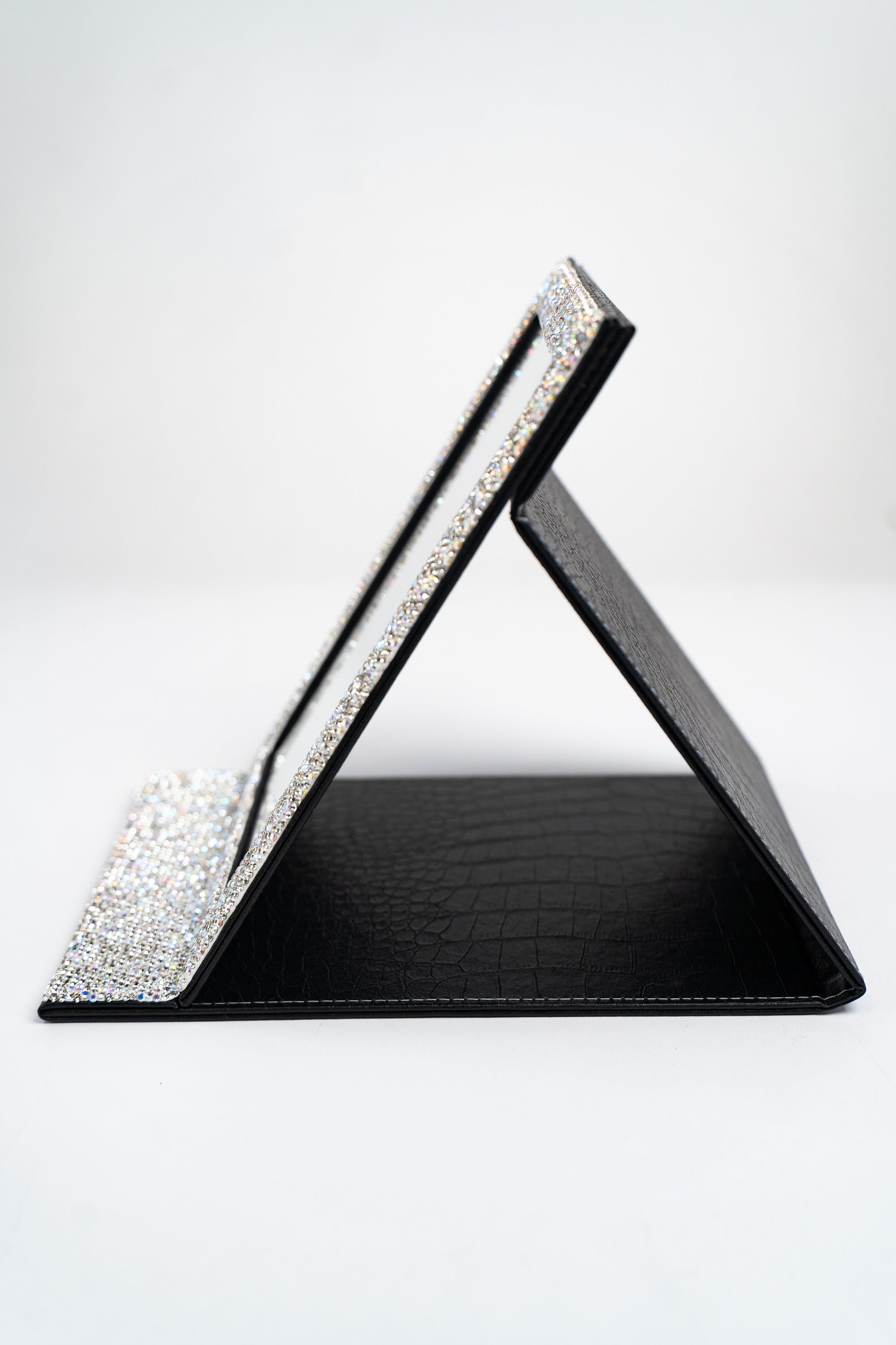 A side view of a large fold-up mirror, in black, with silver and AB rhinestone embellished trim around the mirror